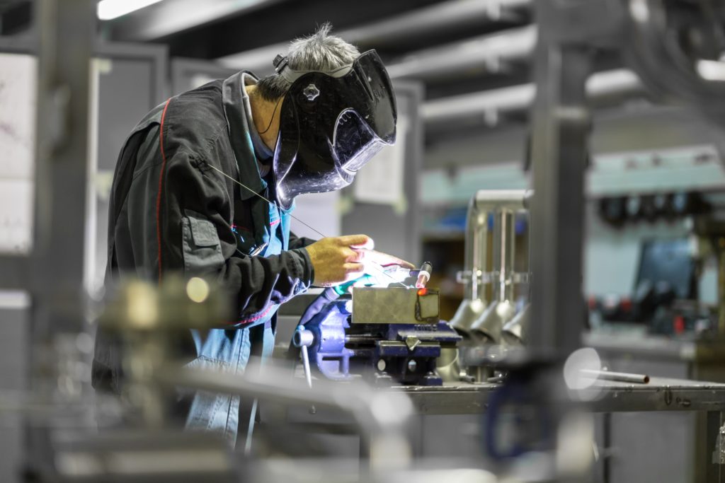 Industrial worker with protective mask welding inox elements in steel structures manufacture workshop.