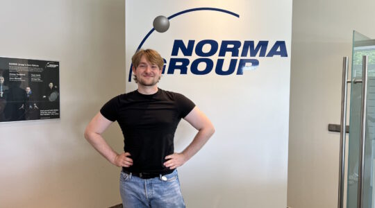 Image of working student Philipp Stiller in front of NORMA Group logo