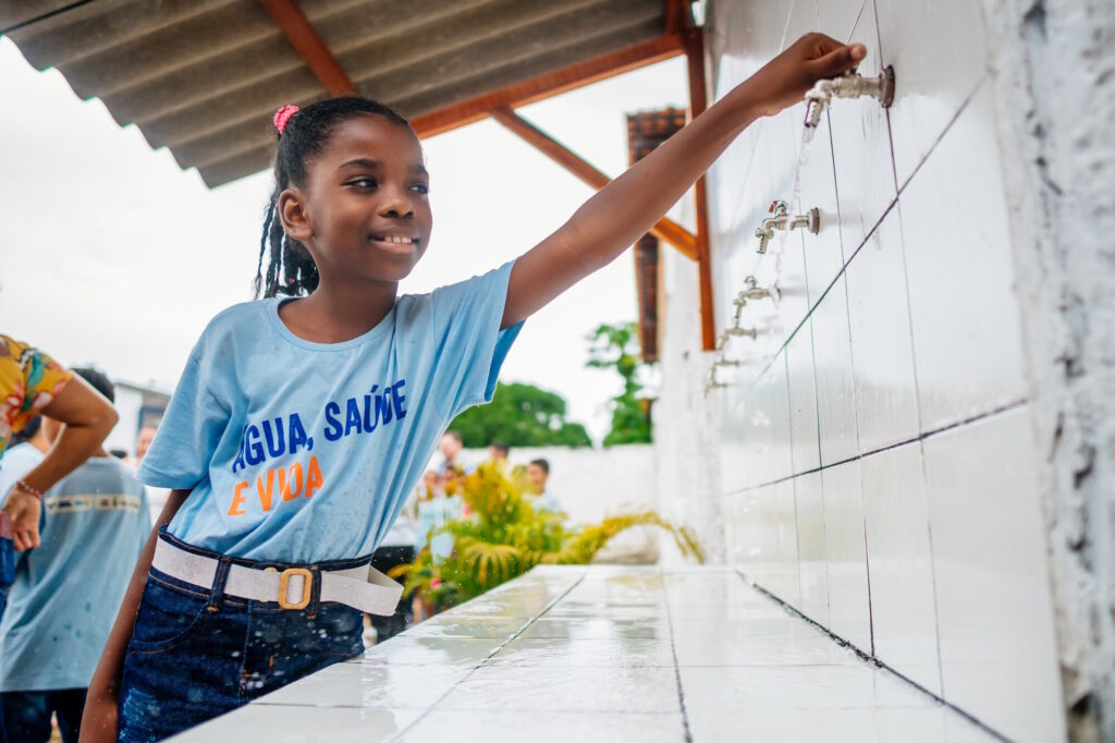 Girl opening a tap in the NORMA Group water supply project